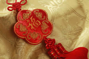 金色布料上帶有金色刺繡的紅色中國結飾品。 — 天秤座 壁紙