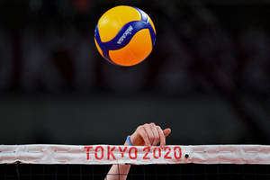一隻手抓住標有 Tokyo 2020 的排球網，一個球懸浮在網上。 — 運動 壁紙