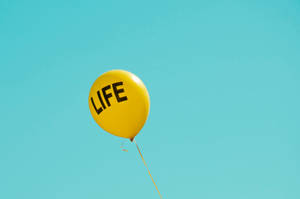 藍天中漂浮著帶有「LIFE」字樣的黃色氣球 — 柔和黃色 壁紙