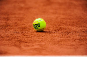 一個黃色網球在紅土球場上，上面有 Roland Garros 2012 字樣。 — 羽球 壁紙