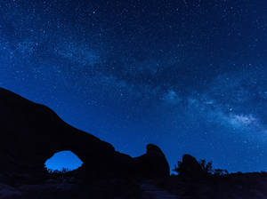 在繁星點點的夜空下，岩石拱門的剪影，銀河系清晰可見。 — 星空動畫 壁紙