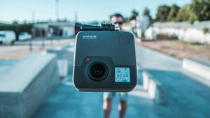 一個GoPro相機指向觀看者，背後有一個人失焦。 — 網路攝影機 壁紙