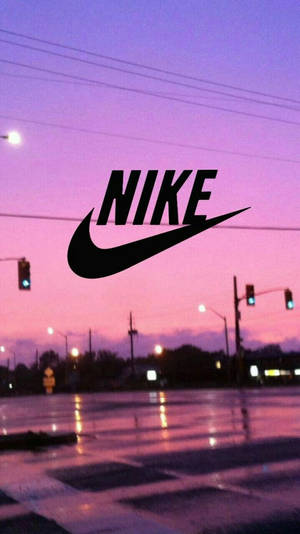 Nike標誌在潮濕的城市街道上，黃昏時分，天空呈現粉紫色，燈光閃爍。 — 嗖嗖聲 壁紙
