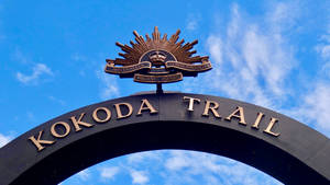 黑色拱門，金色Kokoda Trail文字和軍事徽章，藍天背景 — Pro Display XDR 壁紙