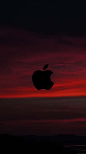 黑色Apple標誌剪影映襯著鮮紅色的日落天空，下方有黑暗的山丘。 — 紅色美學 iPhone 壁紙