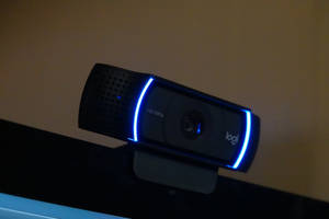在低光環境下，顯示器上的黑色Logitech網路攝影機帶有藍色燈光。 — 網路攝影機 壁紙