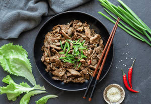 深色表面上，用筷子夾起的炒牛肉，搭配青蔥、芝麻和紅辣椒。 — Burberry 壁紙