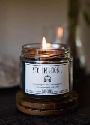 在昏暗房間的木製杯墊上，點燃的蠟燭帶有「STOLEN HOODIE」標籤。 — 午夜 壁紙