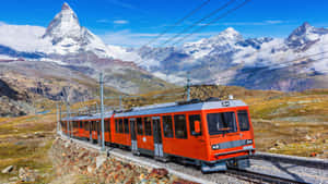 橙色火車行駛在山區鐵路上，背景為馬特洪峰 — 瑞士 壁紙