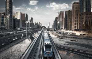 一列現代火車在黃昏時分行駛在高架軌道上，穿過密集的城市景觀。 — 杜拜 壁紙