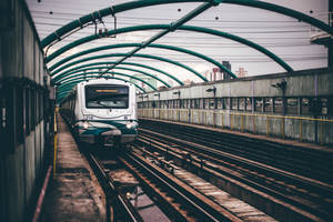 一列火車在都市環境中駛近綠色金屬天篷下的高架軌道。 — 火車 壁紙