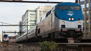 Amtrak火車在城市鐵路調車場中行駛，後面是高樓大廈。 — 火車 壁紙