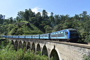 藍色火車在綠色山丘中穿過石拱橋 — 塔橋 壁紙