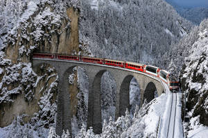紅色火車在雪地山林中穿越石橋