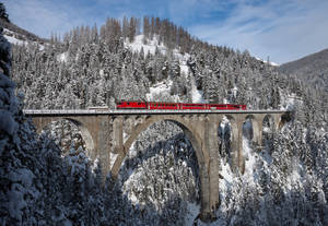 紅色火車在石橋上穿過雪山
