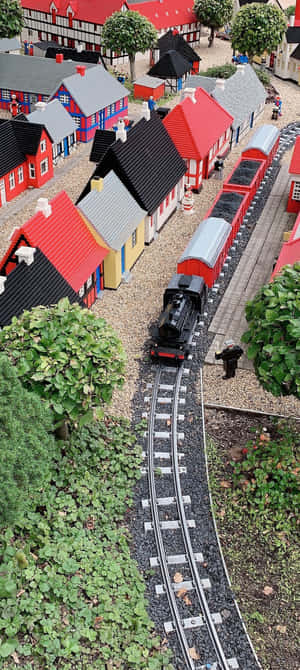 一列黑色蒸汽火車帶著紅色車廂在軌道上穿過一個色彩繽紛的LEGO村莊。 — 海灘 壁紙