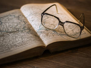 木桌上打開的復古地圖上的黑色框眼鏡。 — 書本美學 壁紙