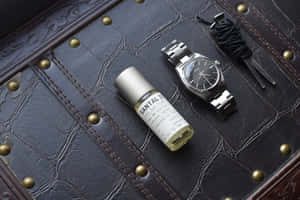 銀色手錶和Santal 33香水瓶在帶有黃銅鉚釘的深色皮革上。 — MacBook Air 壁紙