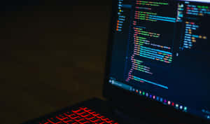 在黑暗房間中，帶有紅色背光鍵盤並在螢幕上顯示彩色程式碼的筆記型電腦。 — 高解析度電腦 壁紙