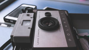 復古Polaroid相機放在藍色桌子上的智慧型手機旁邊。