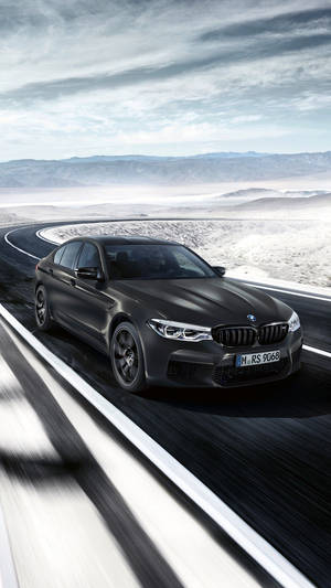 消光黑色BMW M5 RS在沙漠高速公路上奔馳，遠山在望。 — 悟空黑 iPhone 壁紙