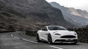 白色Aston Martin在蜿蜒的山路上，有石牆和霧氣籠罩的山峰。 — 奧斯頓馬丁 壁紙
