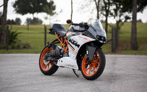 白色和橙色KTM RC機車停在鋪砌道路旁，靠近樹木。 — 巴布風機車 壁紙