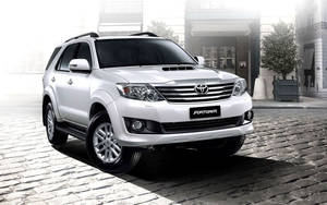 白色豐田 Fortuner SUV 停泊在建築物附近的鵝卵石街道上 — 豐田 壁紙