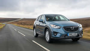 藍色Mazda CX-5在陰天下行駛於鄉村道路，穿過荒野。 — 馬自達 壁紙