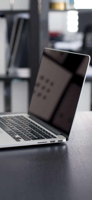現代辦公室環境中深色木桌上的銀色筆記型電腦 — iPhone 15 Pro 壁紙