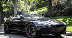 黑色Aston Martin跑車停放在陽光明媚的住宅街道上，周圍有綠樹和草地。 — 奧斯頓馬丁 壁紙