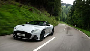 白色Aston Martin在綠意盎然的森林山路中疾馳。 — 超跑 壁紙