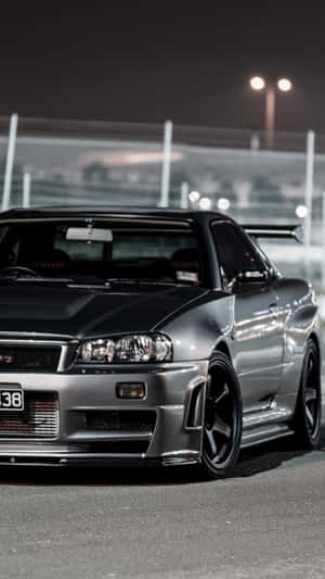 銀色日產Skyline R34在夜間賽道上，在明亮燈光下。 — 日產 Skyline GTR R34 壁紙