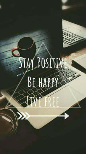 筆記型電腦螢幕顯示「Stay Positive Be Happy Live Free」，木桌上有咖啡杯。 — 快樂 壁紙
