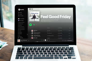 筆記型電腦在窗邊的木桌上顯示 Spotify 的「Feel Good Friday」播放清單。 — Spotify 壁紙