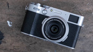 銀色和黑色 Fujifilm 相機在刮花的木質表面上。