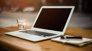 木桌上的銀色筆記型電腦，附有杯水和筆記本。 — MacBook Air 壁紙