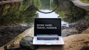 池塘旁木頭上的筆記型電腦，附有勵志名言 work hard travel harder — 筆電 壁紙