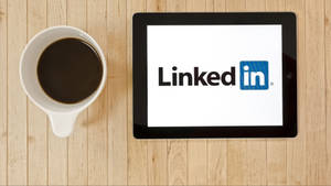 平板電腦顯示LinkedIn標誌，旁邊有一杯咖啡在木上。 — 咖啡美學 壁紙