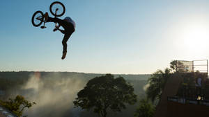 BMX車手在日出時於樹木繁茂的山谷上空進行高跳躍。 — X Games 壁紙