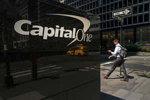 男子在人行道上走過 Capital One 大樓，帶有黃色計程車倒影。 — 男人 壁紙