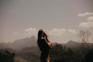 女子以剪影站在山頂上仰望山巒和雲朵。 — Calming 壁紙