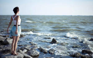 女子站在海邊岩石上眺望水面