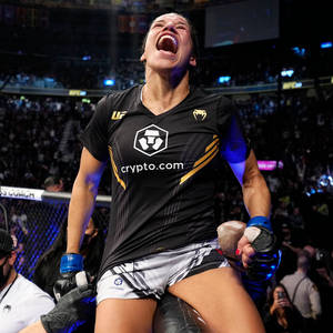 女性MMA拳手在八角籠內慶祝勝利，觀眾歡呼。 — 運動 壁紙