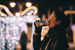 女性在夜晚閃爍的城市燈光下，從節日主題杯中飲用。 — 聖誕燈飾 壁紙