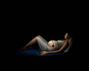 孕婦在黑暗中戴著耳機休息。 — 懷孕 壁紙