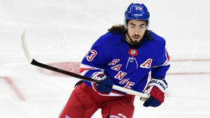 身穿藍紅遊騎兵隊制服的曲棍球選手在冰上持桿滑行。 — 運動 壁紙