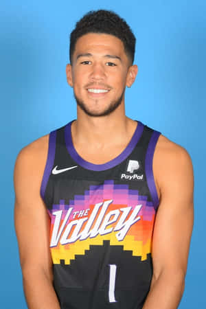 身穿像素球衣的籃球運動員在藍色背景前對鏡頭微笑 — Devin Booker 壁紙
