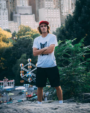 戴紅帽的年輕男子站在岩石上，身後有摩天輪和城市 — 男人 壁紙