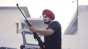 戴紅色頭巾的男子在建築物附近戶外持步槍 — Sidhu Moose Wala 壁紙